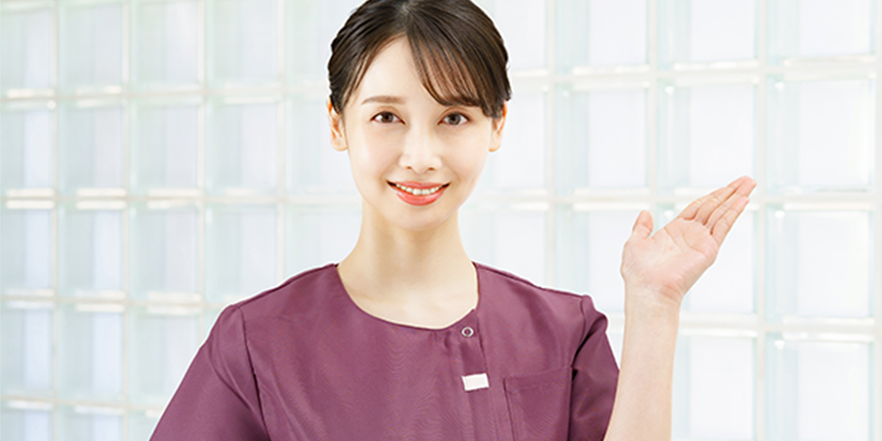 笑顔で案内する女性スタッフ、紫色の制服を着用し明るい雰囲気の施設内で撮影